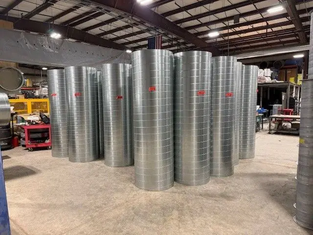 Spiral pipe stock in the DeKalb Mechanical shop, an American flag hanging behind it